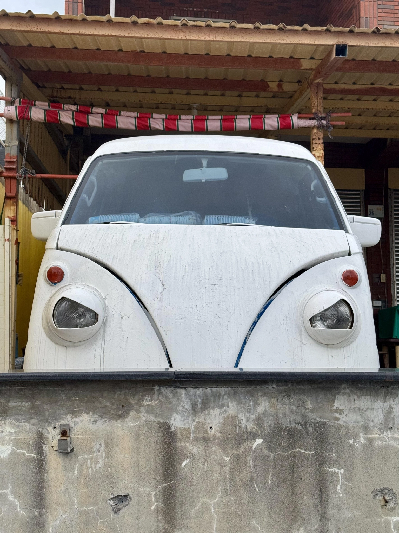A white car behind a very short wall. The front lights are shaped in a way that makes it look like the car is glaring at the viewer.