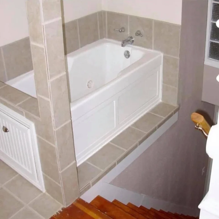 A bathtub set right next to stairs leading downward, without a railing or anything that would stop you from sliding into your death.