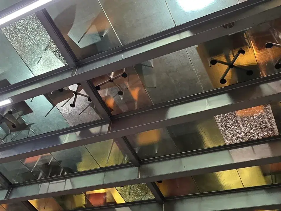 A glass floor viewed from below. It's partitioned in large tiles, 3 of which have shattered but are still holding on.